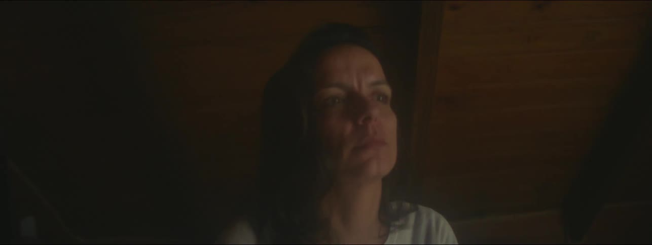 A woman sits up in bed looking anxious with eyes darting around