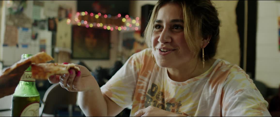 A woman is eating pizza and drinking beer with a friend in a restaurant with a smile on her face