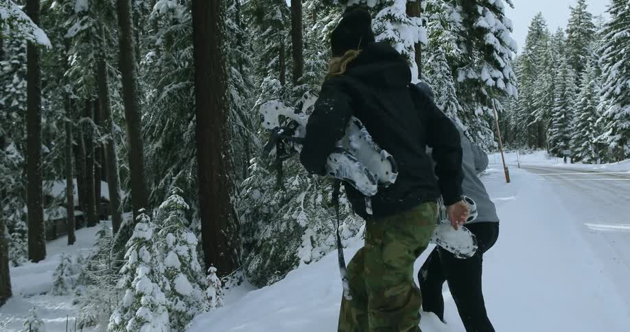 Two women walk off the snowy road into the forest
