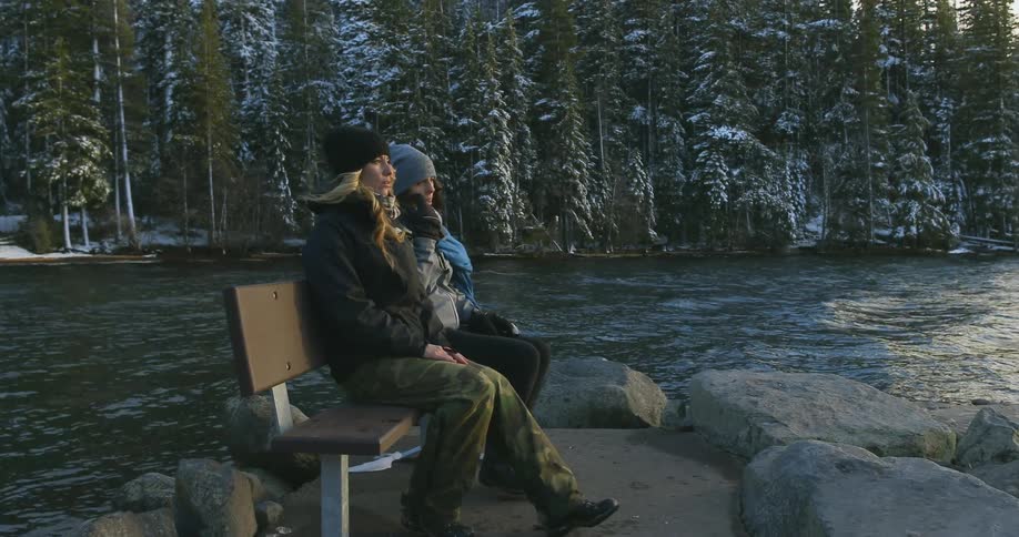 Two women walk over and sit on a bench by the water