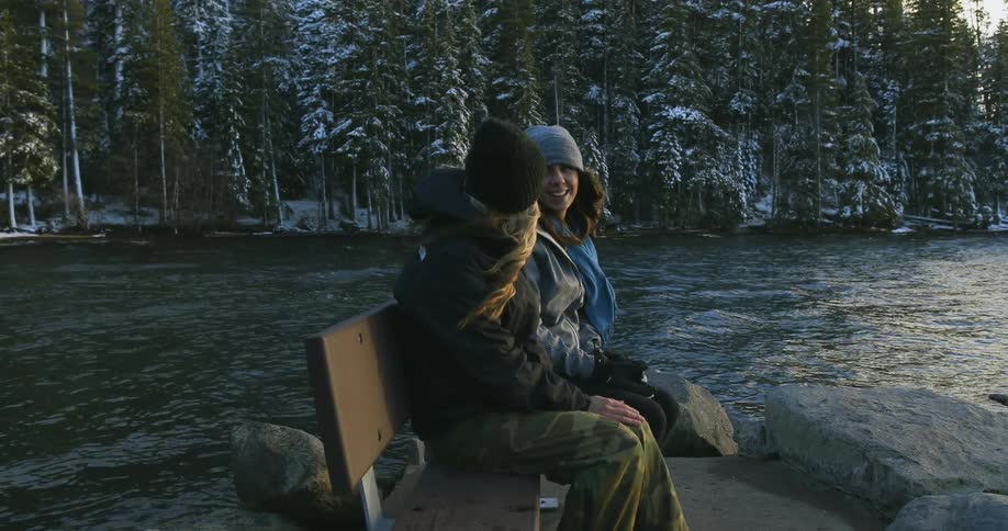 Two women sit on a bench at the end of a jetty on a cold winter day