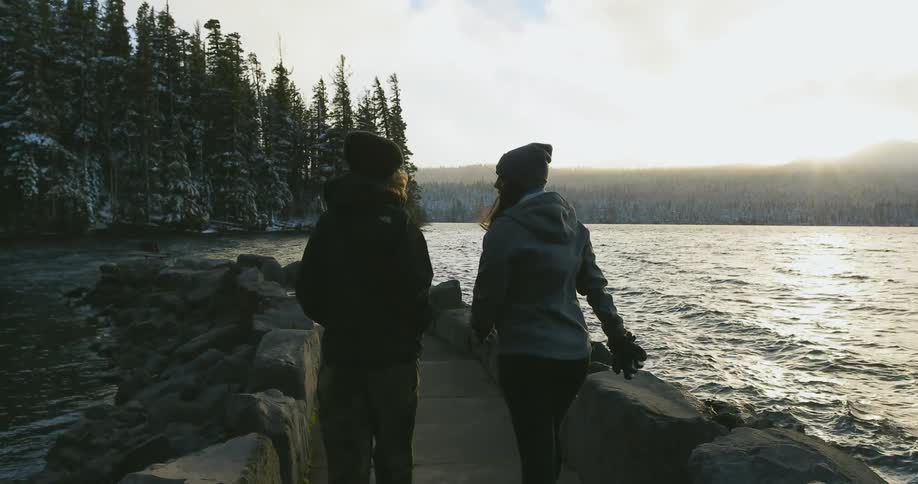 Two women walk down a jetty and overlook a lake on a cold wonter day