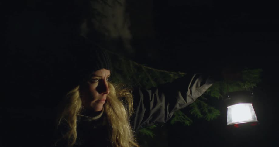 A blonde woman carries a lantern through the forest