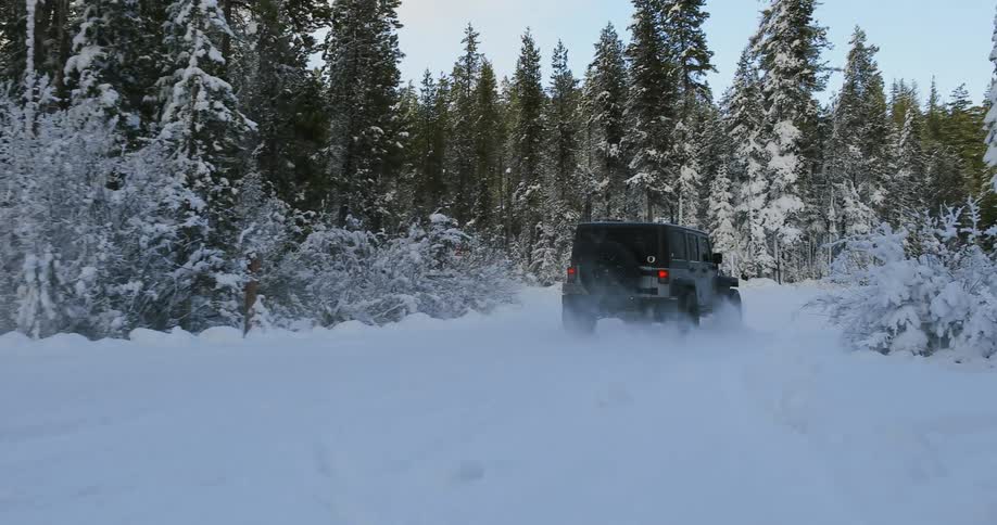 A jeep drives down a snowy country road in the woods
