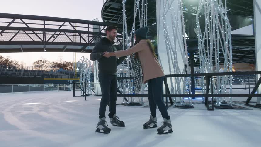 A man and lady are holdinghands while trying to get their balance in ice skates at an outdoor skating rink