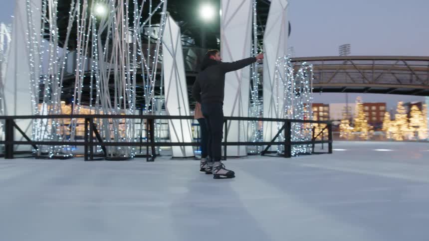 A man and woman are ice skating while holding hands