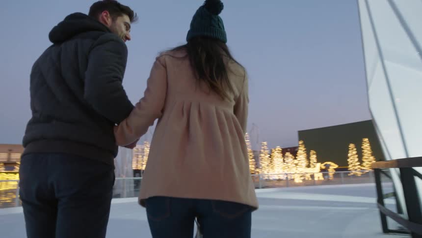 A man and woman are ice skating in a rink surrounded by christmas lights