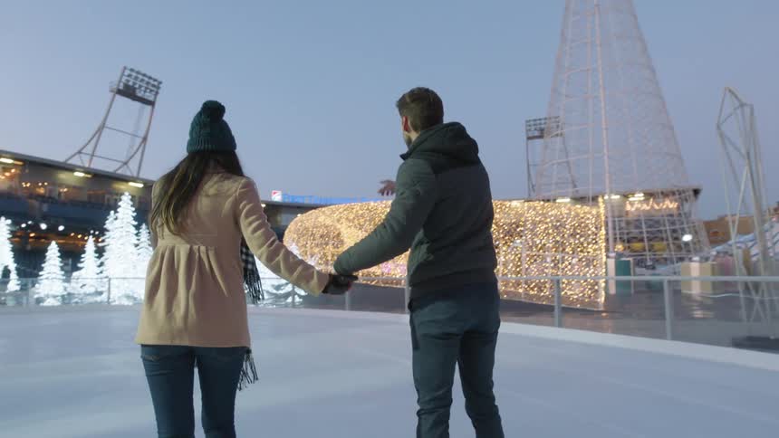 A man and woman hold hands while ice skating outdoors at night
