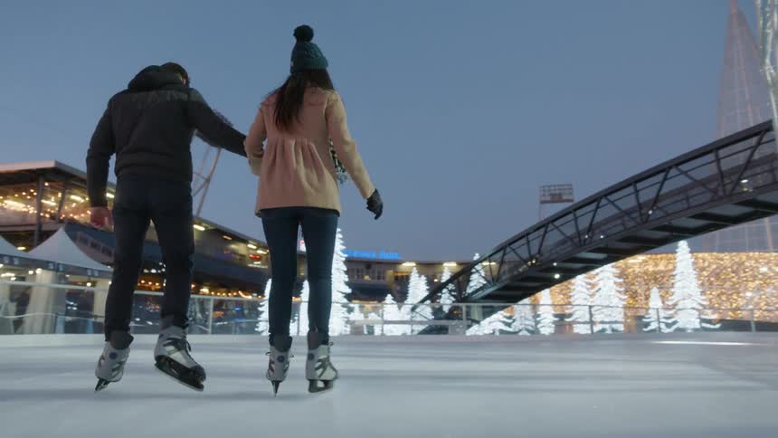 A man and a woman skate together near lit up christmas trees