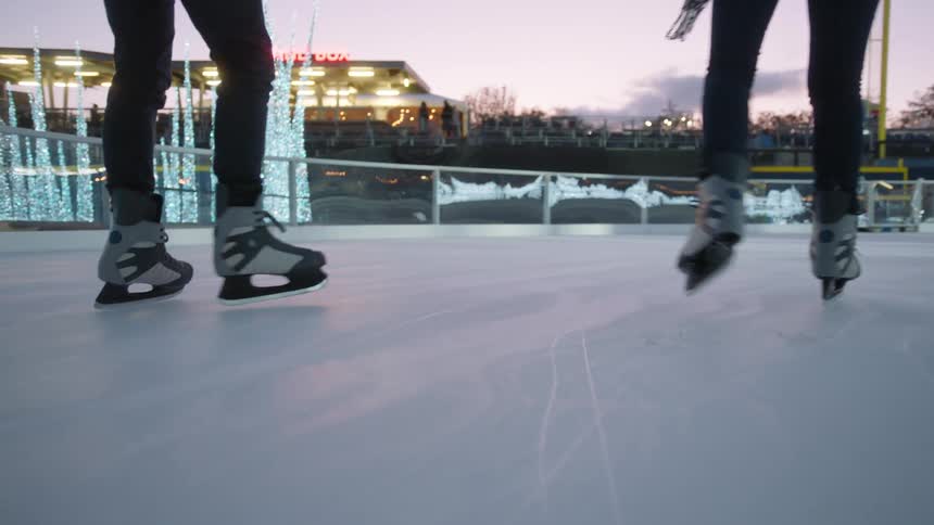 Two people are ice skating on a rink outside