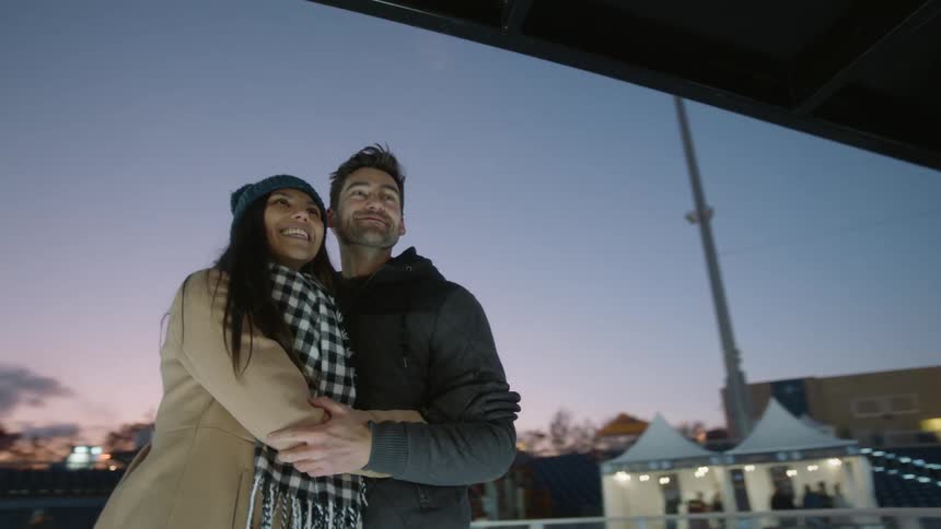 A man and woman hug while surrounded by winter decorations outside