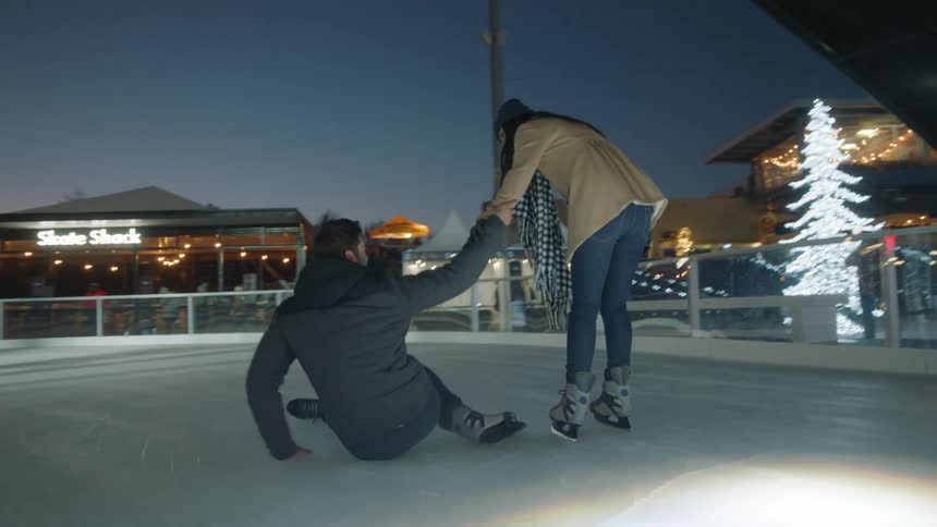 Man falls down as he ice skates with his girlfriend on an outdoor rink