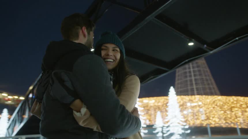 A man and woman hug in an area illuminated by christmas lights