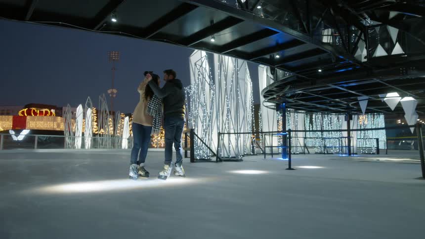 A man and woman ice skate together in a festive christmas display