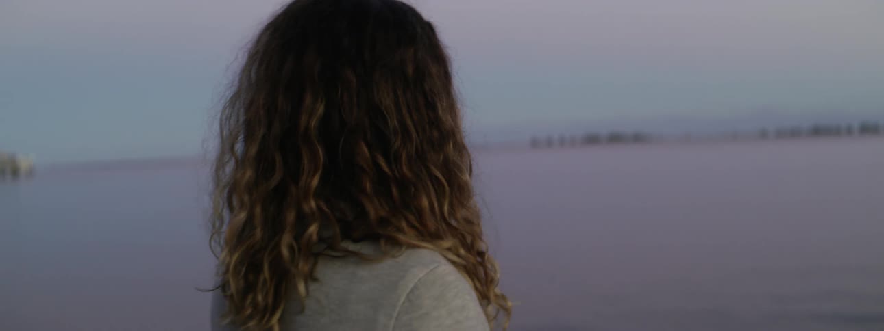 A woman stands outside before a large body of water