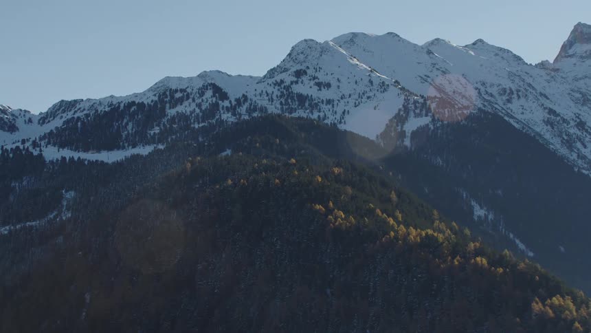 A mountain covered with trees sits next to mountains covered with snow