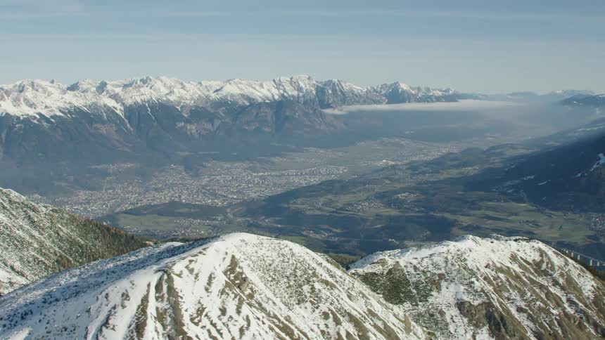 Fog covers valley and obscures town surrounded by snow and forest covered mountains