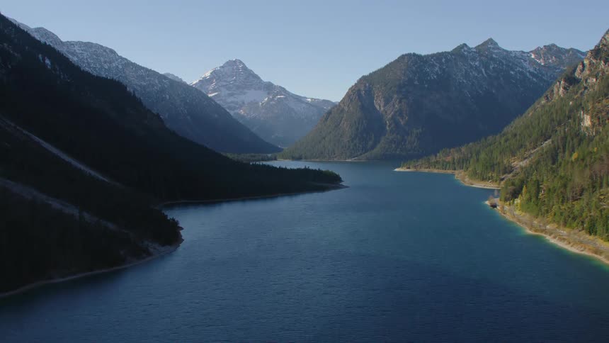 A lake in between mountains that are partially covered in trees and snow