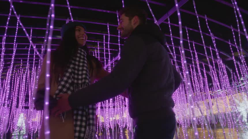 A man and woman dancing together at night outdoors under christmas lights