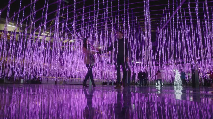 An artistic installation of purple light strings hung from the ceiling with people walking throughout