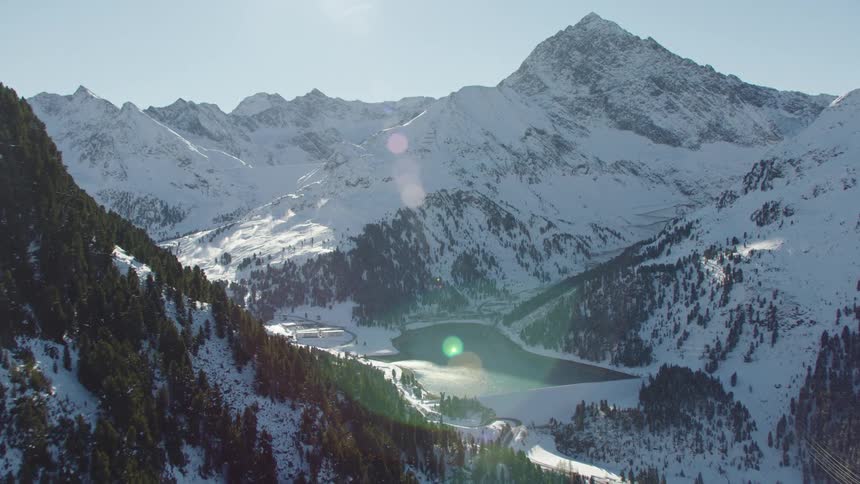 Snow covered forest and mountains surrounds lake on sunny day