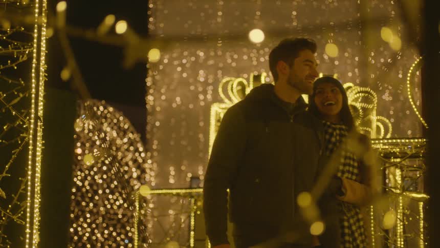 Couple strolling outdoors at night surrounded by holiday lights