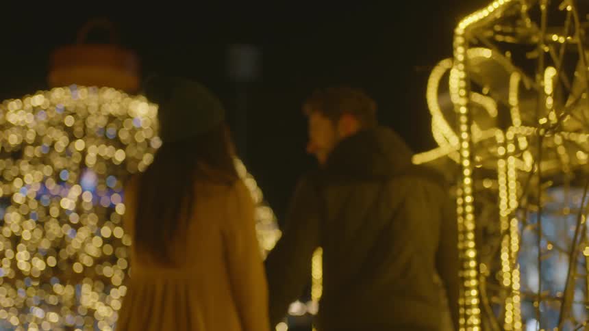 A couple walk hold hands walk through a christmas light display
