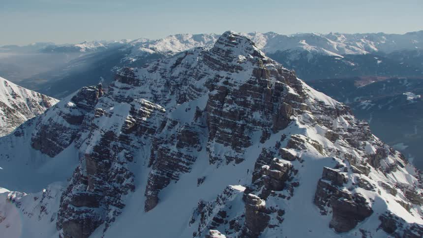 Snow covers rough jagged mountains and slopes of foggy day