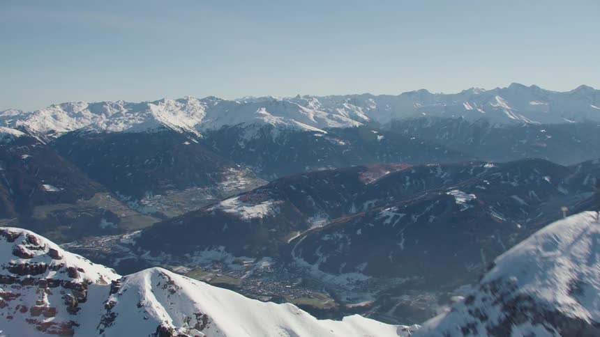 Aerial view moving over a snow covered mountain peak overlooking a valley below
