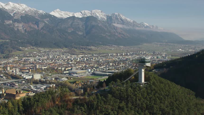 Tower stands on hill near fog covered town occupying valley bordered by snow capped mountains