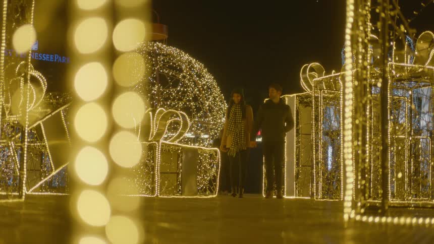 Couple stroll hand in hand through christmas lights display