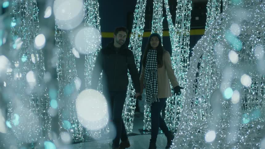 A man and woman hold hands as they walk through a tunnel of lights