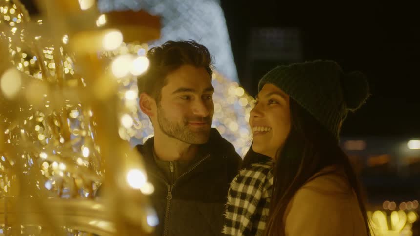 Man and woman look at string christmas lights and smile at each other outdoors