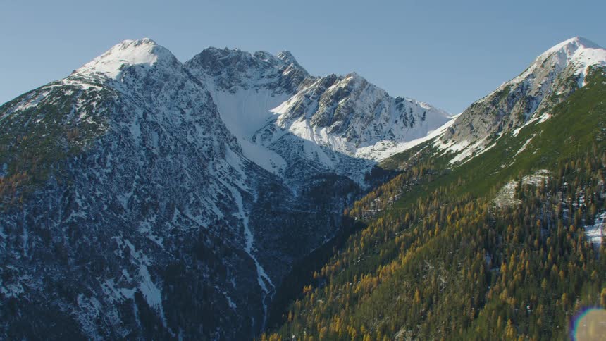 Snow covers one side of a mountain while still green trees line the other