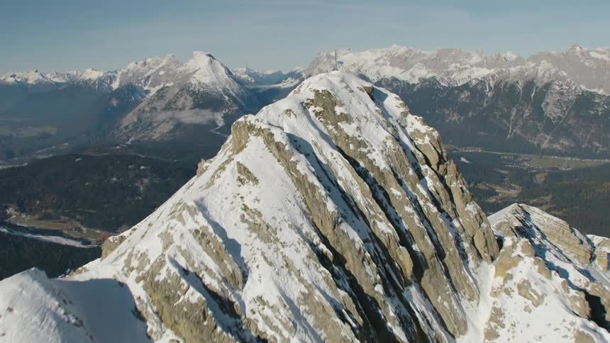 A cross sits on top of a tall mountain covered in snow