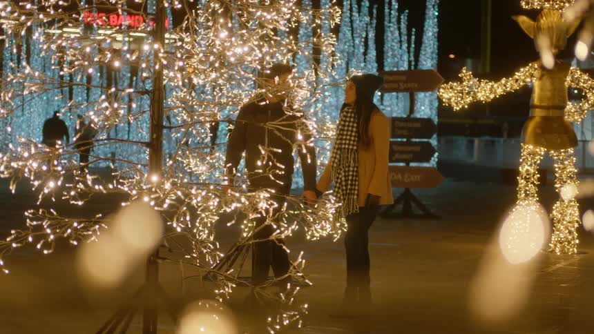 Male and female walk together holding hands through a display of christmas trees made with white twinkling lights at night