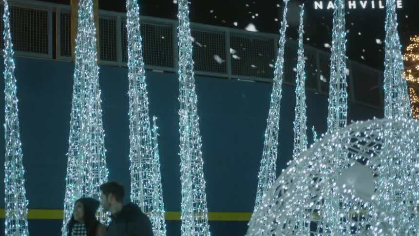 Snow falls as a couple walks through spires of white light at night