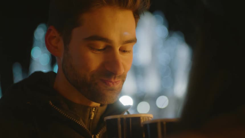 Man drinks coffee and looks at woman at night