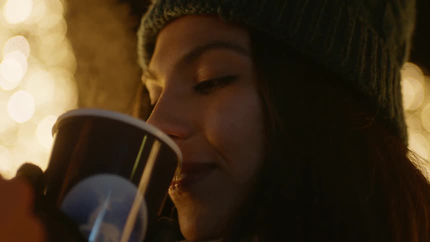 A woman takes a sip of a warm drink from a paper cup and smiles