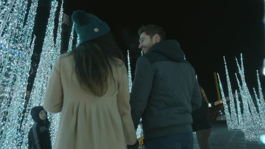 A man and woman hold hands and walk through a lit up area