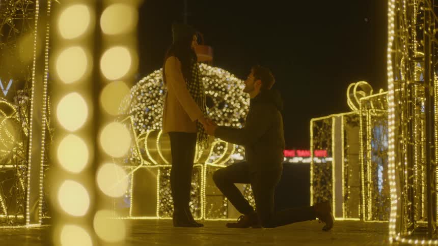A couple is walking through a lighted gazebo and then man gets down on one knee to purpose