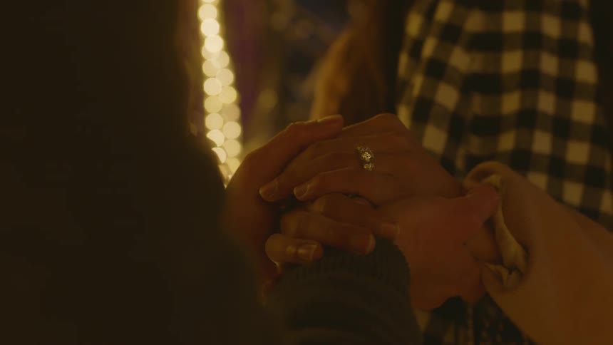 Hand of man placing diamond ring on female finger then holding hands