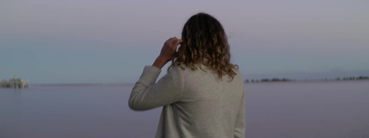 A curly haired person walks near a body of water