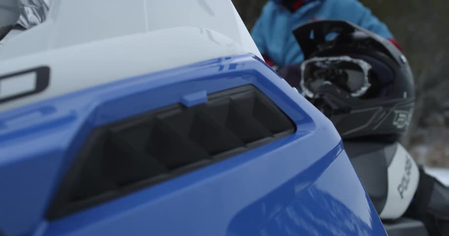 A person is standing behind a snowmobile adjusting his or her gloves
