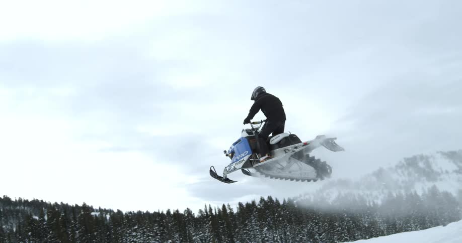 A person riding a blue and white snowmobile coming over the hilltop
