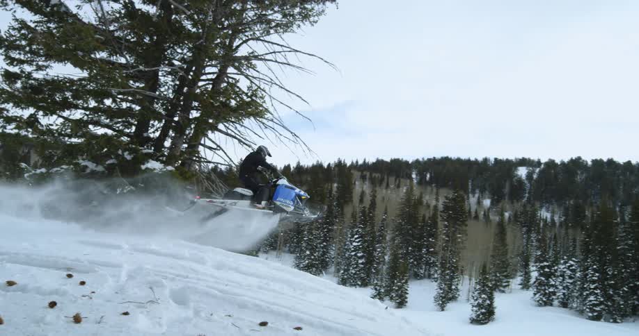 Person riding on a snowmobile flies airborne over a small hill