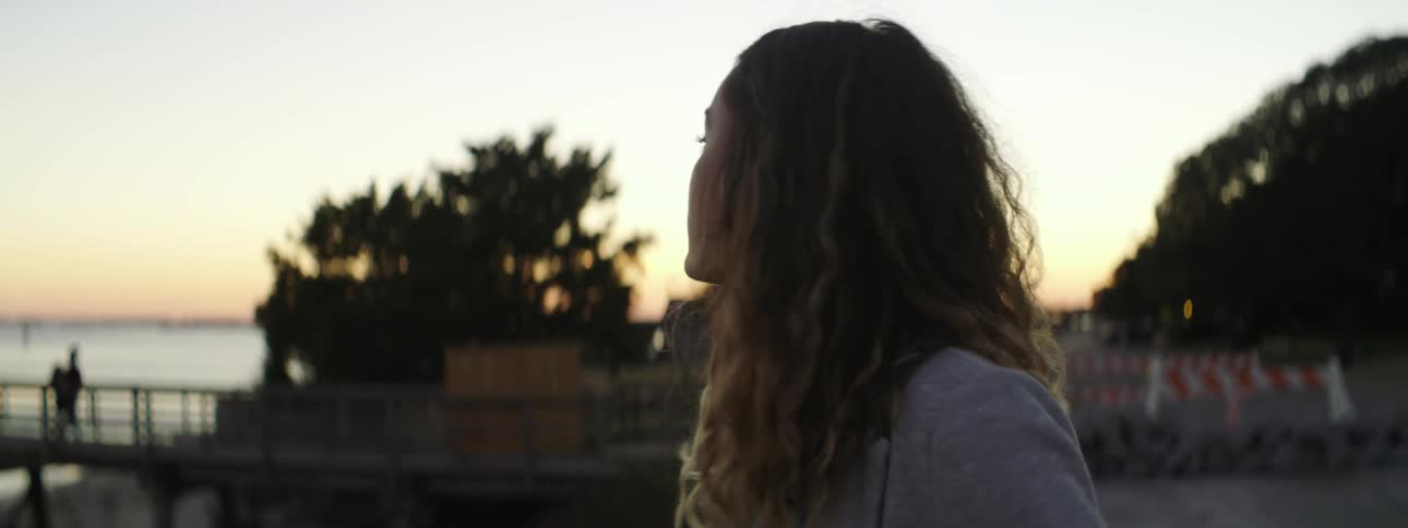A woman looks around outside at sunset