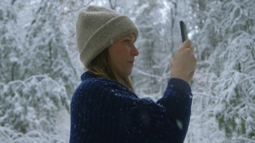 A woman is using her cell phone to take pictures as snow falls