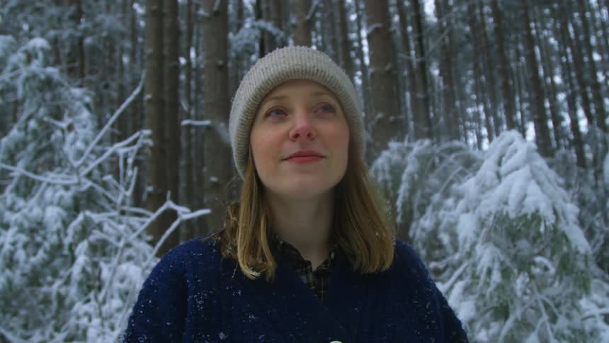 A woman standing in the woods looking at the snowfall