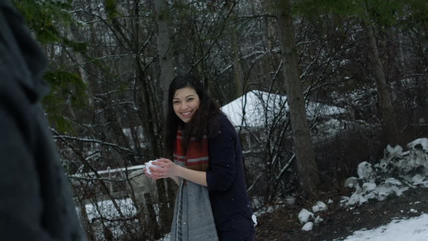 Woman holding a snowball and smiling while standing as the snow falls around her